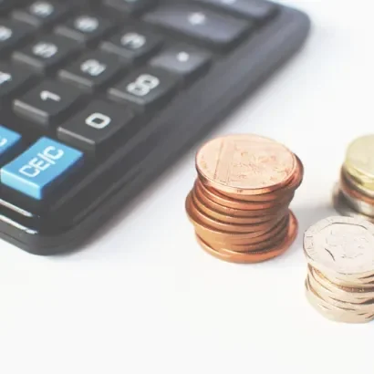 Une calculatrice avec des pièces de monnaie empilées à côté.