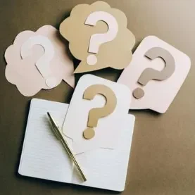 Quatre bulles de dialogue avec des points d'interrogation sur un carnet et un stylo.